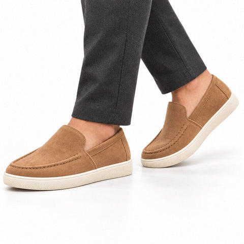 Ellison tan men's casual slip-on shoes with moc toe stitching and white rubber soles, styled with dark trousers for a modern everyday look