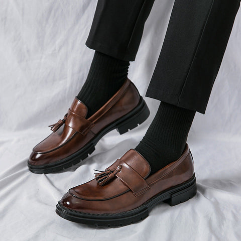 A man in tailored navy trousers and a dark brown leather derby shoe, photographed from the knee down in an office corridor