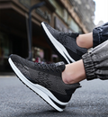 Black athletic shoes with white soles worn by a person on a blurred street background