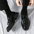 Pair of polished black Sterling men's dress shoes with tassel detail, worn with black socks and trousers, offering discreet height boost and comfortable insoles.