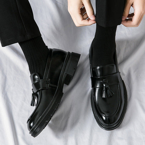 Pair of polished black Sterling men's dress shoes with tassel detail, worn with black socks and trousers, offering discreet height boost and comfortable insoles.