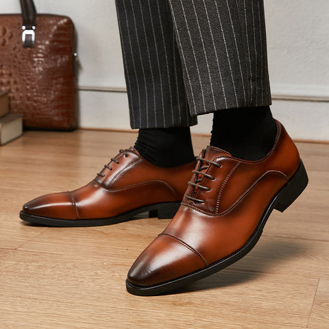 Brown dress shoes worn with striped pants on a wooden floor.