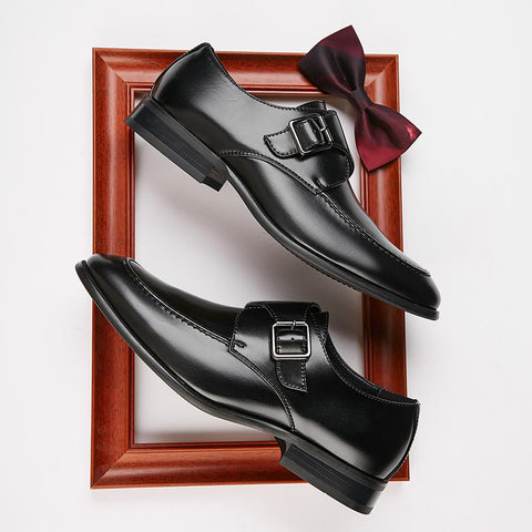 Pair of polished black Lennox shoes featuring sleek buckle detail, displayed inside a wooden frame alongside a burgundy bow tie, representing discreet height boost and formal elegance.