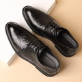 Pair of black leather dress shoes on a beige surface