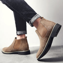 Brown suede ankle boots worn with rolled-up jeans on a light gray background