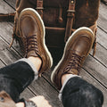 Brown leather boots worn with a backpack on a wooden floor