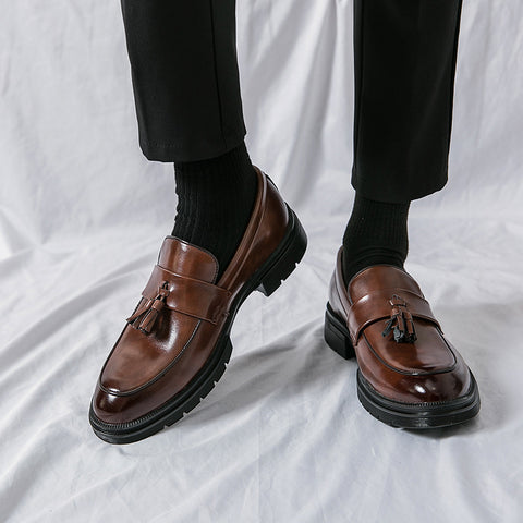 Pair of polished brown leather tassel loafers named Sterling with discreet height-increasing soles, worn with black socks and black trousers for a formal, stylish look.