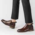 Pair of polished brown Wellington boots with discreet hidden heel lift, worn with black tailored pants, showcasing modern elevation and comfortable insoles for men's dress shoes.