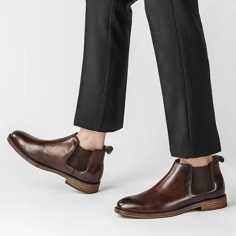 Pair of polished brown Wellington boots with discreet hidden heel lift, worn with black tailored pants, showcasing modern elevation and comfortable insoles for men's dress shoes.