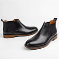 Pair of black leather Wellington boots with discreet height increasing design, elastic side panels, and brown stacked heels offering comfort and style for men.