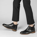 Pair of black leather Wellington boots with hidden heel, worn with black tailored pants, highlighting modern style and discreet height boost for men.
