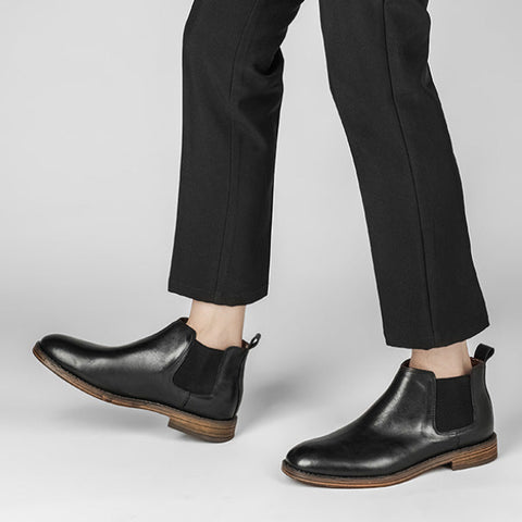 Pair of black leather Wellington boots with hidden heel, worn with black tailored pants, highlighting modern style and discreet height boost for men.