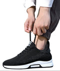 Person tying the laces of a black athletic shoe with a white sole on a plain background