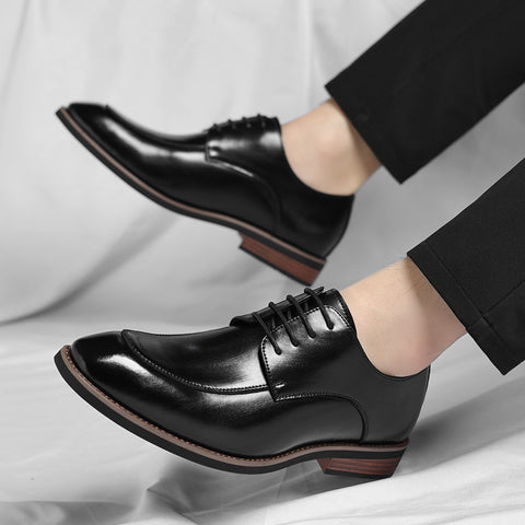 Black dress shoes with brown soles worn by a person on a light gray background