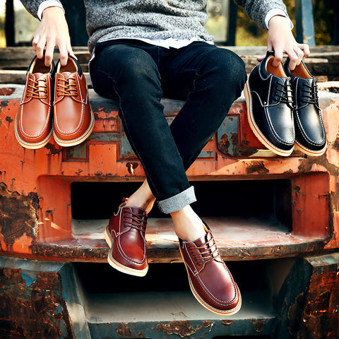 Person sitting on a rusted metal surface holding two pairs of shoes, one brown and one black. Wearing burgundy height boosting shoes.