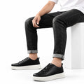 Hawthorn black men's casual shoes with lace up styling and thick white soles shown with rolled black jeans in a clean studio setting