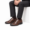 Prestige brown leather men's dress shoes with lace-up styling and brogue detailing shown on a seated man for a polished professional look and discreet height boost