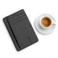 The Modern Cardholder in black textured leather with multiple card slots displayed beside a cup of espresso on a white background